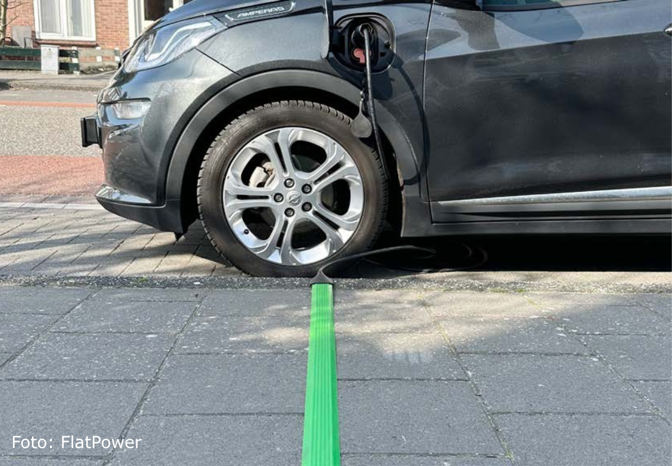 Elektrische auto met platte laadkabel over stoep.