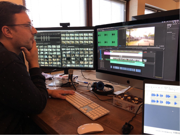 Man aan bureau met twee beeldschermen bewerkt de audio bij een video
