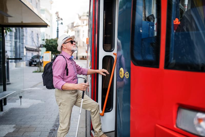 Oudere man met geleidestok stapt in een bus