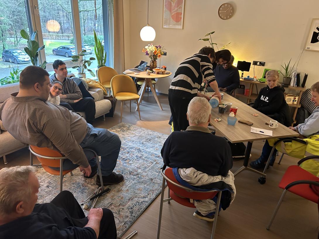 Foto van de groep ervaringsdeskundigen die bij elkaar komen in een huiselijke setting.