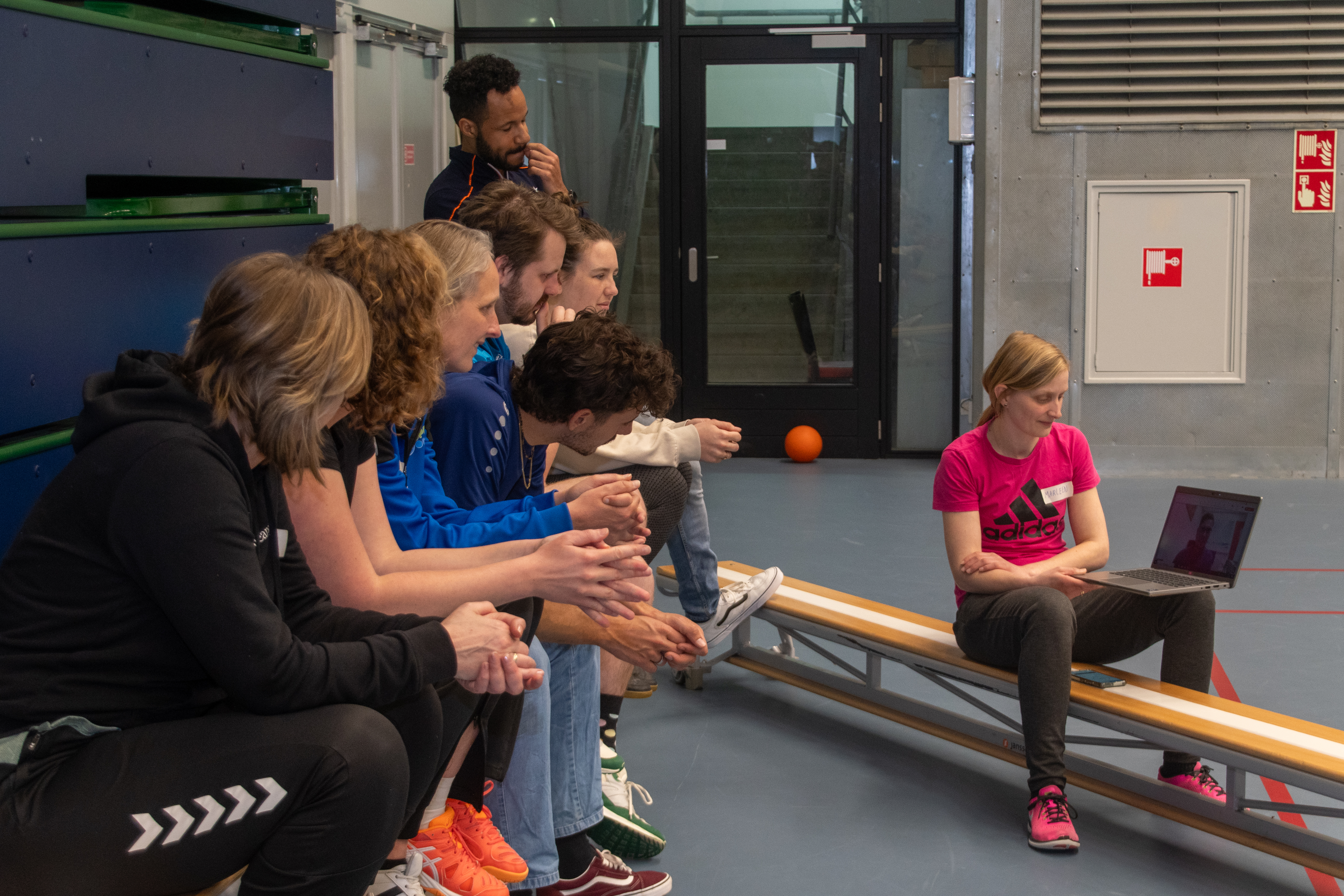 Foto praktische gedeelte trainingsdag buurtsportcoaches. Deelnemers zitten op een bank en kijken naar een computerscherm waar een ervaringsdeskundige vragen beantwoordt.